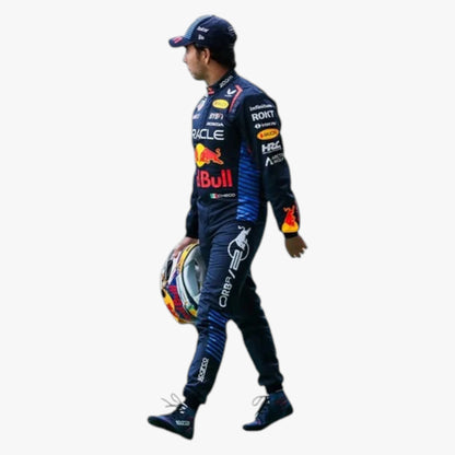 A racer in a dark blue Red Bull Racing suit walks while holding a colorful racing helmet, shown against a plain white background.