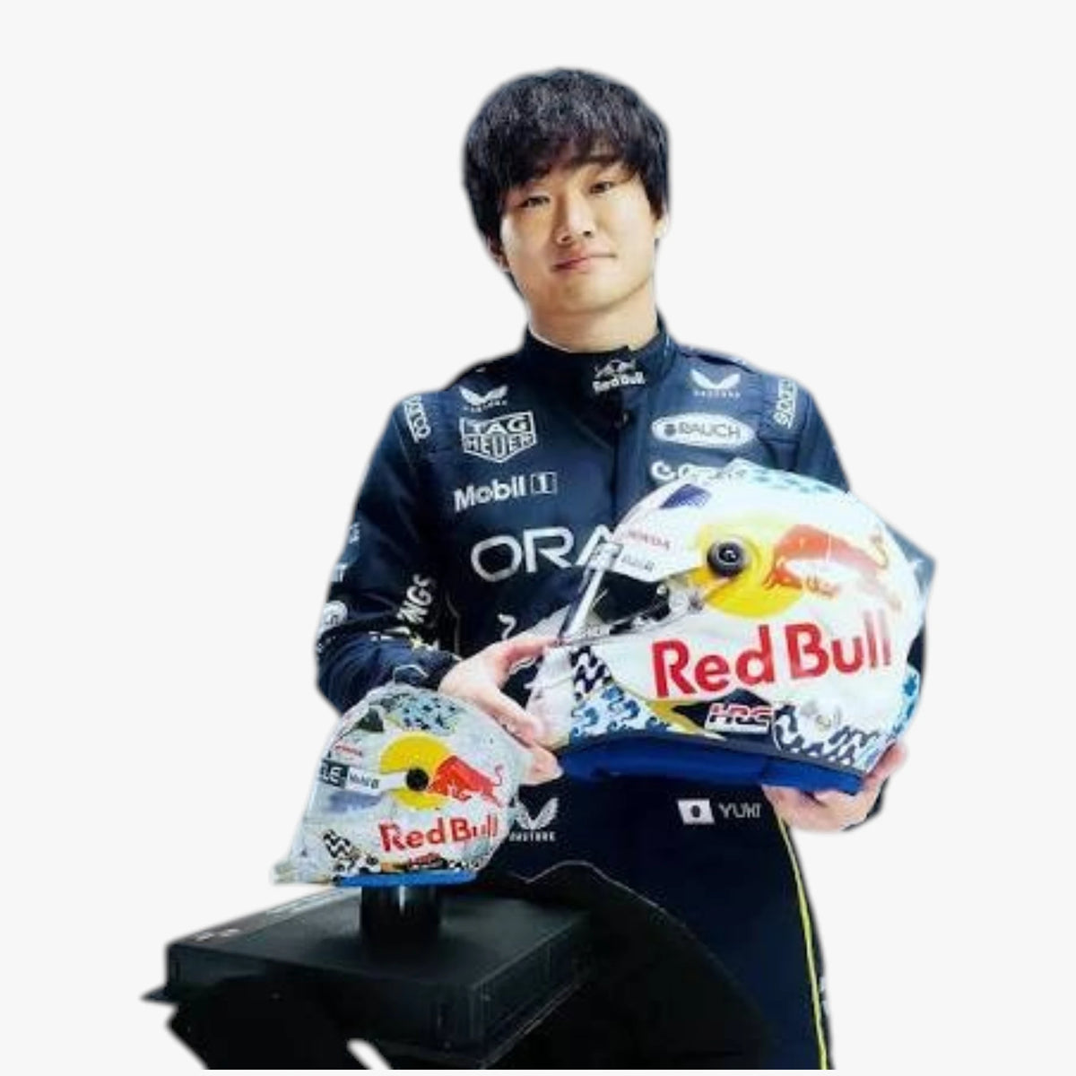 A man in a Red Bull racing suit holds two Red Bull racing helmets, one large and one smaller, against a plain white background.
