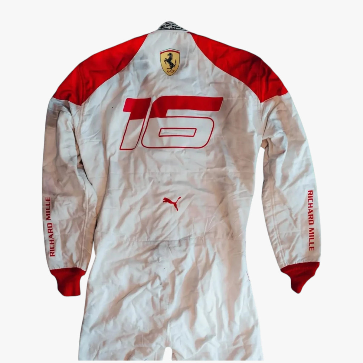 A white and red long-sleeve racing suit with '16' printed on the back, featuring the Ferrari shield logo on the neck, a Puma logo on the lower back, and 'RICHARD MILLE' printed down both sleeves.