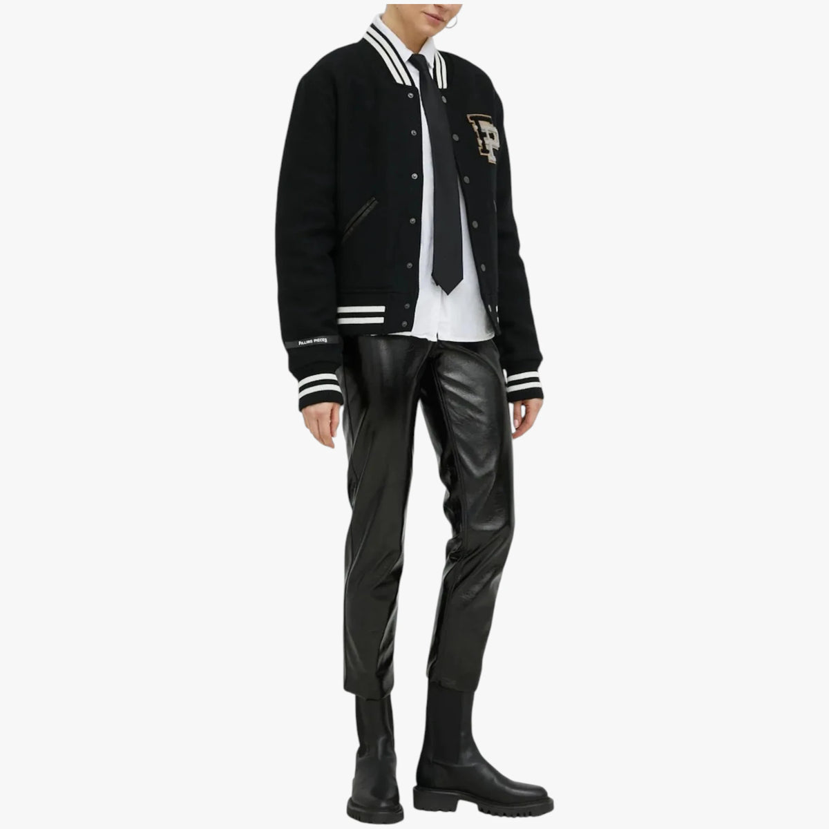 A model wearing a black varsity jacket with white stripes, a white shirt, a black tie, black faux-leather pants, and black boots, shown against a plain light gray background.
