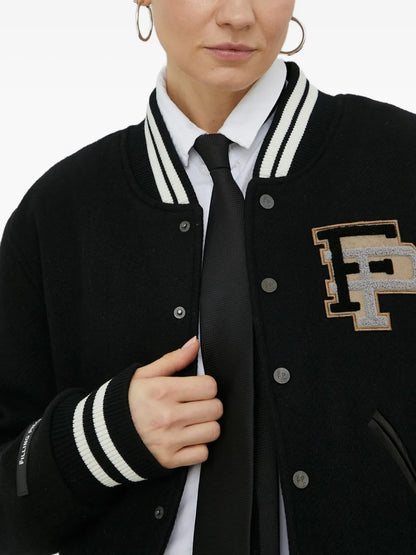 A close-up of a person wearing a black varsity-style jacket with white striped ribbed trim, a large embroidered letter 'F' patch on the chest, and silver buttons, styled over a white collared shirt and black tie.
