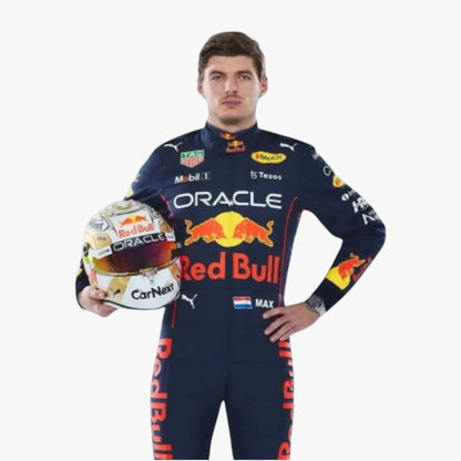 A man in a Red Bull racing suit holds a Red Bull helmet against a plain light gray background. The suit features prominent Oracle, Red Bull, Puma, and other sponsor logos.