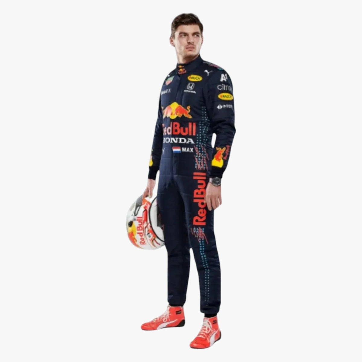 A man wearing a Red Bull Racing team racing suit stands against a light gray background, holding a Red Bull Racing helmet. The suit is dark navy blue with prominent red, yellow, and white sponsor logos, and he is wearing red and white racing shoes.