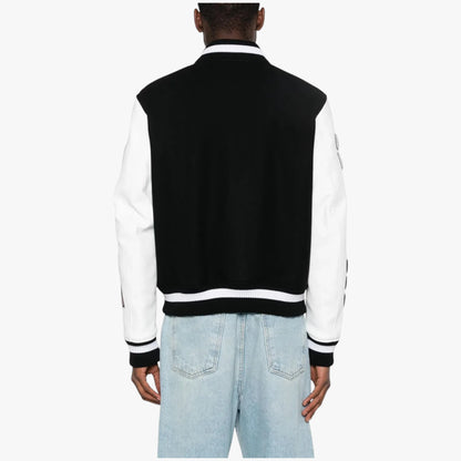 A person shown from the back wearing a black and white varsity-style jacket with light blue jeans, photographed against a plain light gray studio background.