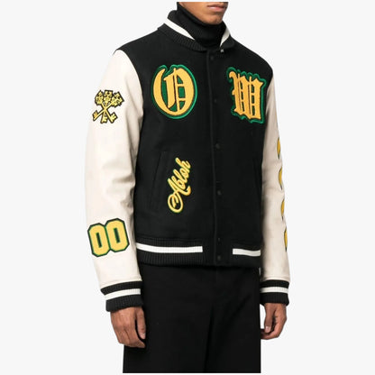 A black and off-white varsity jacket with green and yellow embroidered details, worn by a model against a light gray background.