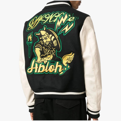 A person wearing a black and cream varsity jacket, shown from the back. The jacket features a large embroidered graphic of a horned warrior holding a torch, with the words 'Off We Go Abolish' in green and yellow.